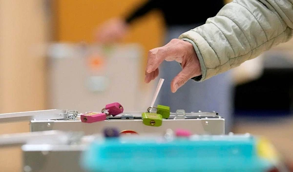 A voter casts a ballot in the lower house elections as representatives of a local election administration commission observes at a polling station Sunday, Oct. 31, 2021, in Tokyo