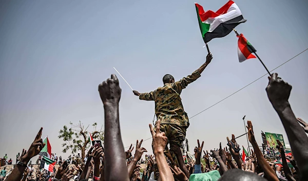 A Sudanese soldier joins protestors shouting slogans and waving national flags during a protest outside the army complex in the capital Khartoum on April 18, 2019 (Credit: AFP)