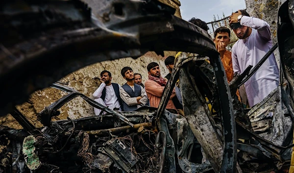 Relatives of the Ahmadi family gather around the incinerated husk of a vehicle targeted and hit by a US drone strike that left 10 dead, Kabul, Aug 30, 2021 | Getty