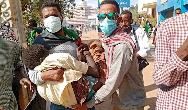 Sudanese protesters rush to the aid of a wounded protester after security forces fired tear gas during a rally in the capital Khartoum on December 19, 2021 (AFP)