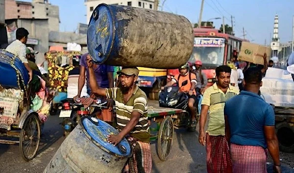 A laborer transporting plastic drums along a busy street in Dhaka (AFP)