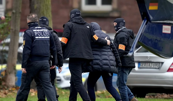 An suspect, second right, is escorted from a police helicopter by police officers after the arrival for a questioning at the federal prosecutor's office in Karlsruhe, Germany, Wednesday, Dec. 7, 2022 (AP Photo/Michael Probst)