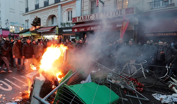 Members of Kurdish community stand next to a barricade on fire as they clash with police officers at the crime scene where a shooting took place in Paris, Friday, Dec. 23, 2022 (AP Photo/Lewis Joly)