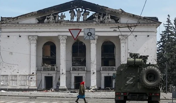 =A woman walks past an armoured vehicle Mariupol (Reuters)