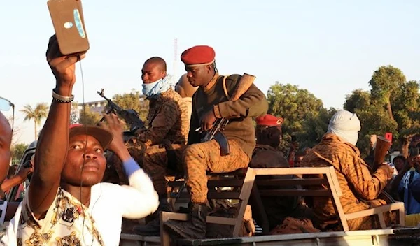 A man uses his mobile phone beside army soldiers after they deposed President Kabore in Ouagadougou, Burkina Faso, January 24, 2022 (Reuters)