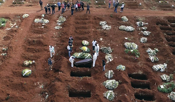 Workers wearing protective gear lower the coffin of a person who died of COVID-19 into a grave in Sao Paulo, Brazil (AP)