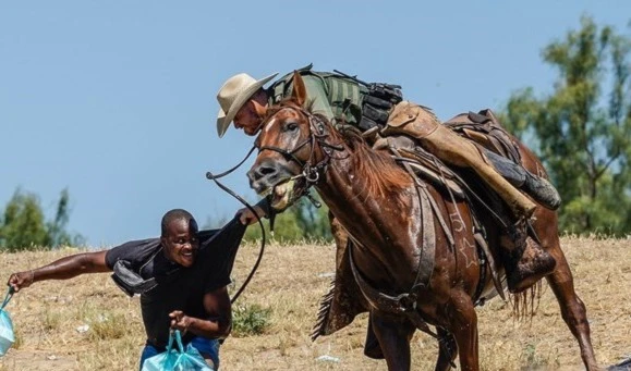 A United States border patrol agent on horseback using a rein against a Haitian migrant, Texas (AFP)