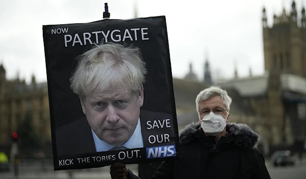 protester holds a placard with an image of British PM Boris Johnson calling him Partygate