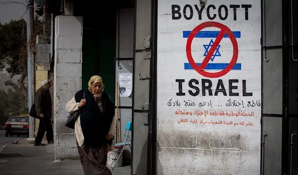 A Palestinian woman walks by a sign calling for a boycott of the Israeli occupation in Beit Lahm, occupied West Bank, on February 11, 2015