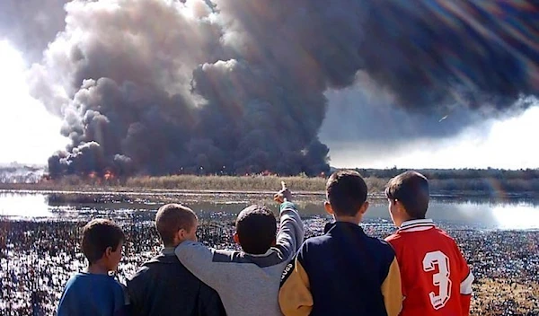 A group of Iraqi boys gather to watch smoke billowing from burning oil on the outskirts of the town of Baiji, north of Baghdad, March 15, 2005 (Reuters)