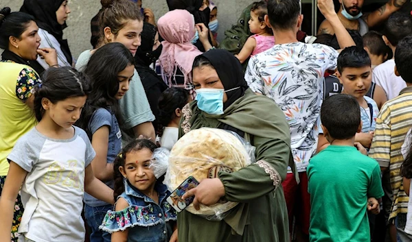 A woman leaves a bakery with a bag of bread as people wait for their turn, in the neighbourhood of Nabaa in the Lebanese capital Beirut's southern suburbs ANWAR AMRO AFP