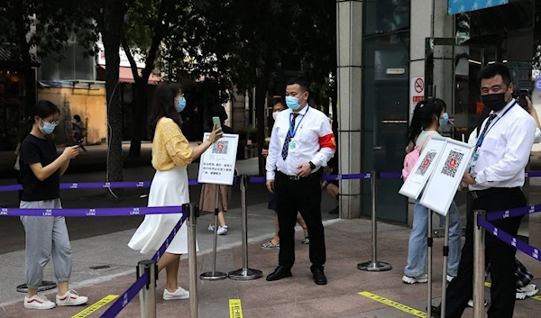 A woman shows her health status on a phone to a security guard, at an entrance of a shopping mall in Beijing, China August 23, 2021. REUTERS/Tingshu Wang