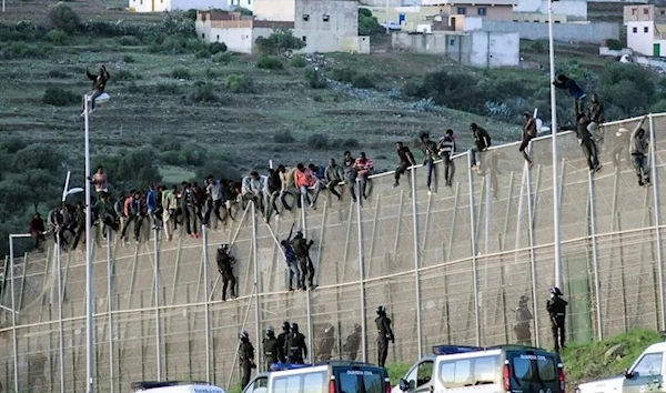 African migrants sit at the top a border fence, as Spanish Civil Guard officers stand underneath, during an attempt to cross into Spanish territories, between Morocco and Spain's north African enclave of Melilla on 16 October, 2014. (Reuters)