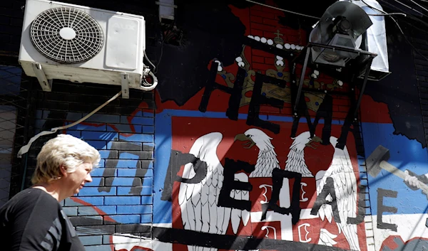 A woman walks in front of a graffiti that shows maps of Kosovo and Serbian coat of arms and flag, that reads: ''No surrender!'', in northern, Serb-dominated part of ethnically divided town of Mitrovica, Kosovo, Aug. 17, 2022