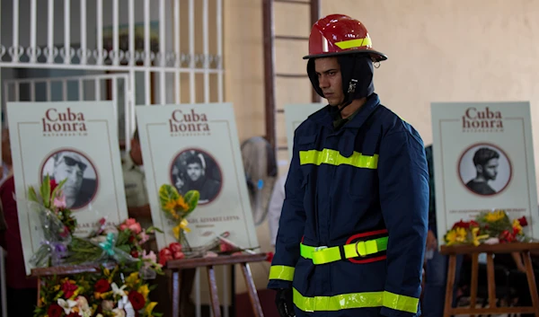 A firefighter walks past photos and caskets of those who died in the fires at the Matanzas Supertanker Base during a funeral ceremony inside the Firefighters Museum in Matanzas, Cuba, Friday, Aug. 19, 2022 (AP Photo)