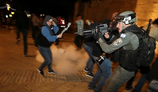 Israeli occupation police stand in position as a stun grenade explodes by the gate to al-Quds' Old City (Ammar Awad/Reuters)