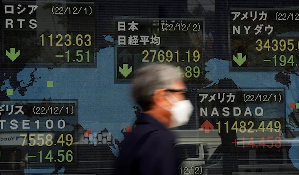 A man walks by monitors showing Japan's Nikkei 225 index and other countries' stock market indexes at a securities firm in Tokyo, Friday, Dec. 2, 2022 (AP Photo/Hiro Komae)