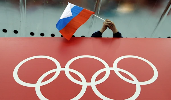 A Russian flag is held above the Olympic Rings at Adler Arena Skating Center during the Winter Olympics in Sochi, Russia on Feb. 18, 2014 (AP Photo/David J. Phillip, File)