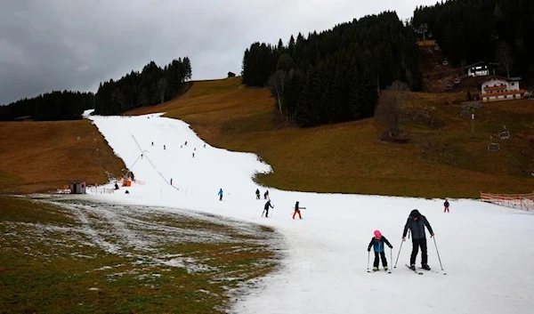 Skiers pass on a small layer of an artificial snow slope between grassland amid warmer-than-usual winter temperatures in the Alps in Filzmoos, Austria, January 5, 2023. REUTERSPIX