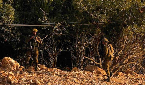 Israeli soldiers take positions alongside the border wall and fence with Lebanon as seen from the Lebanese side of the Lebanese-Palestinian border area in the southern village of Marwaheen, Lebanon, October 12, 2023 (AP)