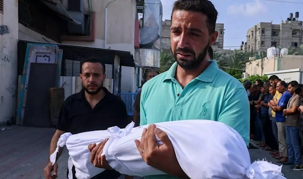 A Palestinian man carries the body of his child, killed in overnight Israeli shelling, during a funeral in Khan Younis, in the southern Gaza Strip, on 10 October 2023. (AFP)