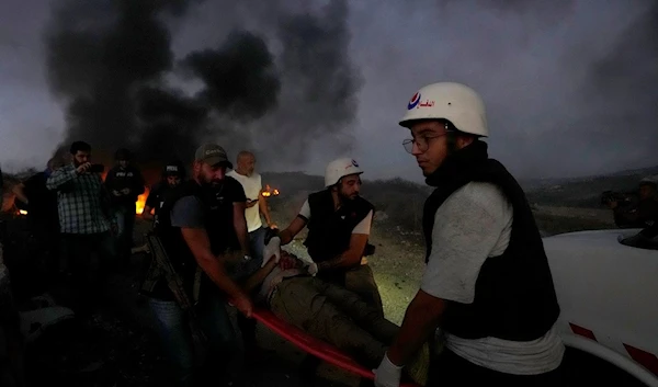 Civil Defence workers and a Lebanese security officer carry a journalist who was injured by Israeli shelling, at Alma al-Shaab, south Lebanon, Friday, Oct. 13, 2023 (AP)