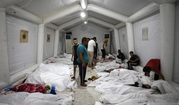 People stand over bodies of Palestinians killed in Israeli airstrikes on the Ahli Arab hospital in central Gaza after they were transported to Al-Shifa hospital, on October 17, 2023. (AFP)