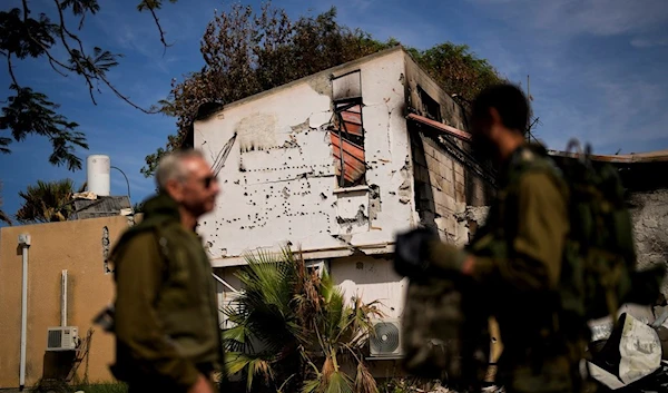 Soldiers walk next to a house damaged by Hamas militants at Kibbutz 'Kissufim' in southern occupied Palestine, October 21, 2023 (AP)