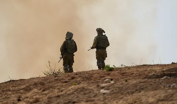 Israeli Occupation Forces stand next to a burning field near the border with the Gaza Strip, in southern Israel, Tuesday, Oct. 24, 2023. (AP)