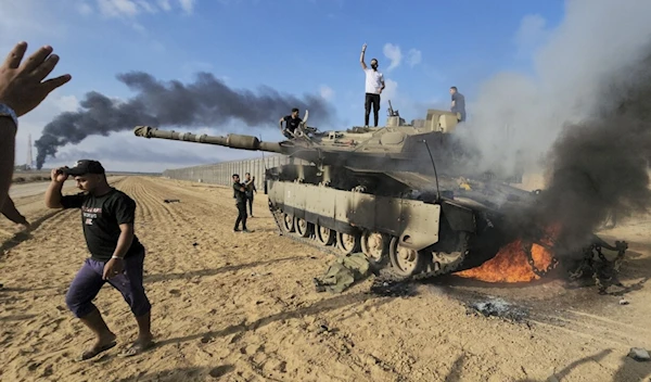 Palestinians celebrate by a destroyed Israeli tank at the Gaza Strip fence east of Khan Younis southern on Saturday, October 7, 2023. (AP)