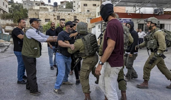 A masked Israeli settler stands by while Palestinians and Israeli soldiers scuffle during clashes in the town of Huwara in the occupied West Bank. (AFP)