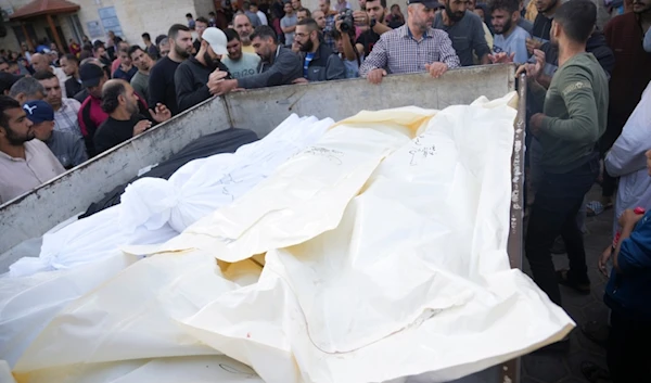 Palestinians stand around their relatives martyred in the Israeli bombardment of the Gaza Strip, in front of the morgue in Deir al Balah, November 11, 2023 (AP)