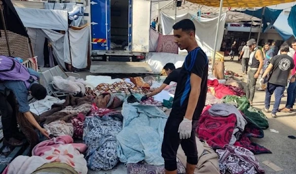 A man is looking for the bodies of family members killed in bombardment that hit a school housing displaced Palestinians, as they lie on the ground in the yard of al-Shifa Hospital in Gaza City on Nov. 10, 2023. (AFP)