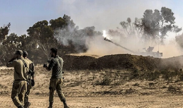 Israeli invading soldiers walk near a stationed self-propelled artillery howitzer firing rounds from a position near the border with the Gaza Strip on November 6, 2023. (AFP)