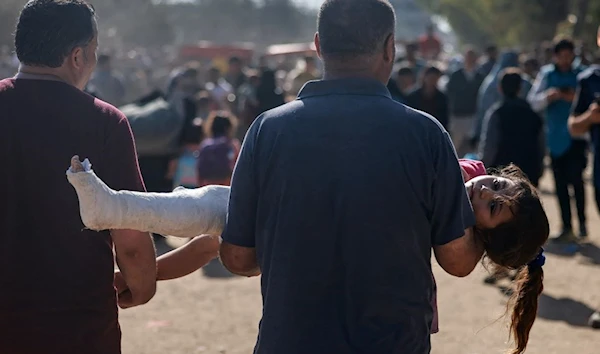 A father carries his injured child as Palestinians are being forcibly displaced from Gaza City and other parts of northern Gaza, walk along a road leading to the southern areas of the enclave. [AFP]