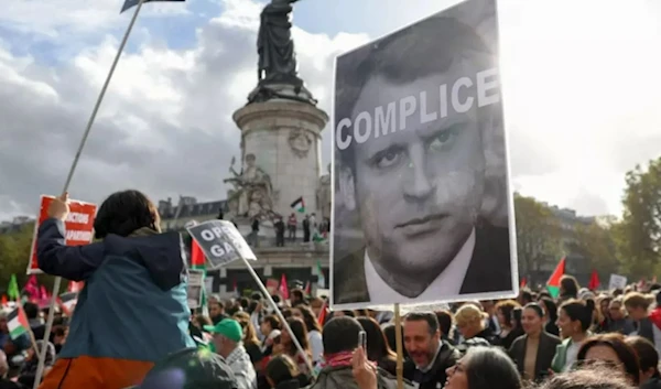 Protesters hold up a sign condemning French President Emmanuel Macron at a rally in Paris on 22 October 2023 (AFP)