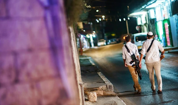 Armed Israeli settlers walk through the street with guns in the mixed Arab-Jewish town of al-L, occupied city of al-Lydd, Friday, May 28, 2021. (AP)