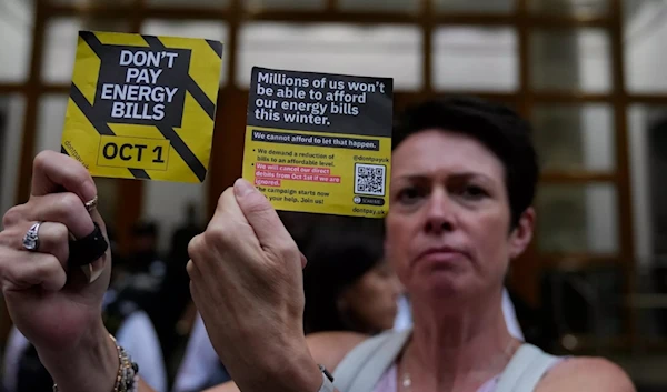 A demonstrator holds up two cards as they protest outside the British energy regulator Ofgem (AP)