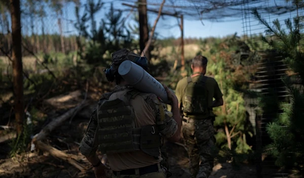 A Ukrainian soldier carries a shell towards a howitzer on the front line in the outskirts of Lyman, Donbass region, Tuesday, Aug. 15, 2023 (AP Photo/Bram Janssen)