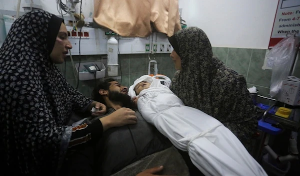 A Palestinian woman shows the body of her grandchild, her father after it was killed in the Israeli bombardment of the Gaza Strip outside a morgue in Rafah, Tuesday, Dec. 19, 2023. (AP Photo/Hatem Ali)