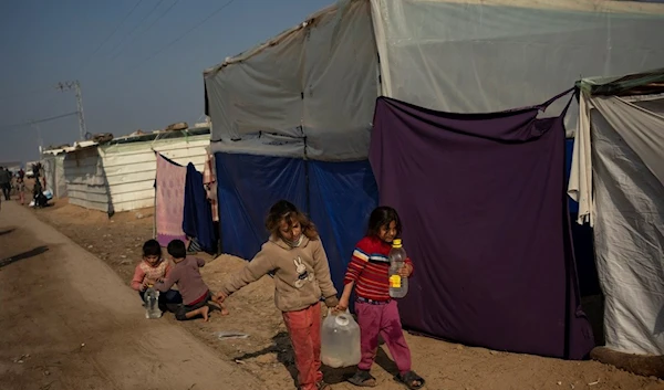 Palestinian children displaced by the Israeli occupation's genocide in the Gaza Strip carry water in the makeshift tent camp in the Muwasi area, occupied Palestine, on Monday, Dec. 18, 2023. (AP)