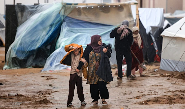 Palestinians walk under the rain at a camp for displaced people in Rafah, in the southern Gaza Strip where most civilians have taken refuge on December 13, 2023 (AP)