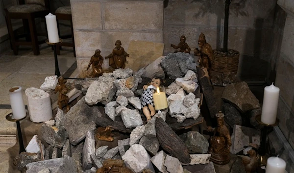 An installation of a scene of the Nativity of Christ with a figure symbolizing baby Jesus lying amid the rubble, in reference to Gaza, inside the Evangelical Lutheran Church in the West Bank town of Beit Lahm, Sunday, Dec. 10, 2023 (AP)