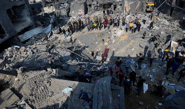 Palestinians look at the destruction of the al-Gatshan family building after an Israeli strike in Nuseirat refugee camp, central Gaza Strip, on December 18, 2023 (AP)