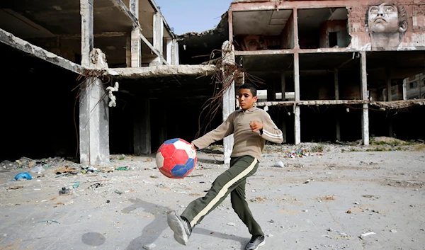 A boy plays football next to a mural painted by Palestinian artist Ali Al-Jabali on the remains of a building in April 30, 2019. (AP)