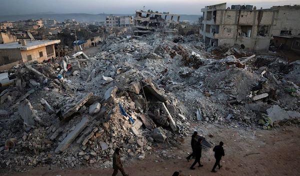 People walk past collapsed buildings following a devastating earthquake in the town of Jinderis, Aleppo province, Syria, Thursday, Feb. 9, 2023 (AP Photo/Ghaith Alsayed)