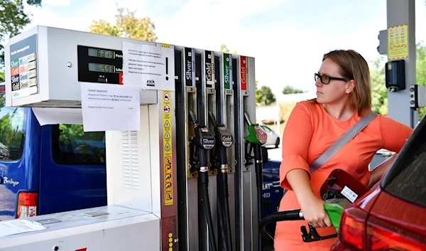 Hungarian motorist fills up her car while reading the banner which says "we ask you to fill up to maximum 20 litres of 95 petrol at a time" in Budapest, Hungary, Wednesday, Aug. 10, 2022 (AP Photo/Anna Szilagyi)