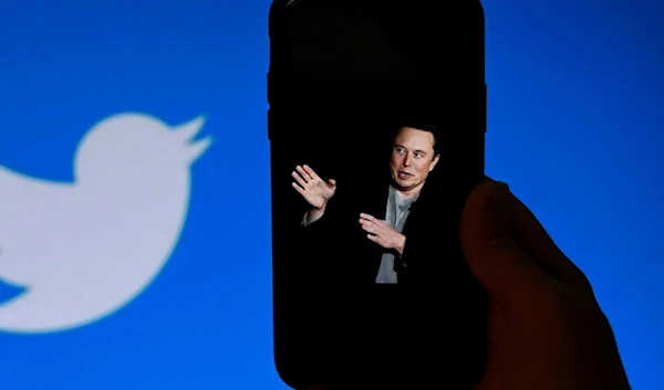 In this illustration photo taken on October 4, 2022, a photo of Elon Musk is displayed on a phone with the Twitter logo shown in the background (AFP)