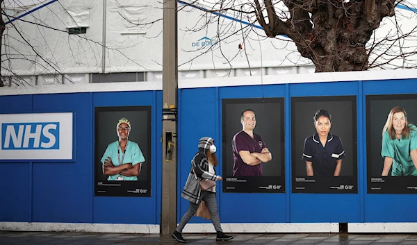 A person walks past images of National Health Service (NHS) workers displayed on hoardings outside a temporary field hospital at St George's Hospital, amid the coronavirus disease (COVID-19) outbreak in London, Britain, January 8, 2022 (Reuters).