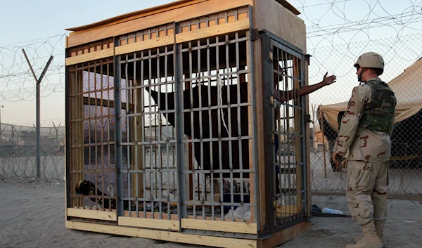 A detainee in an outdoor solitary confinement cell talks with a military policeman at the Abu Ghraib prison on the outskirts of Baghdad, Iraq, June 22, 2004 (AP)